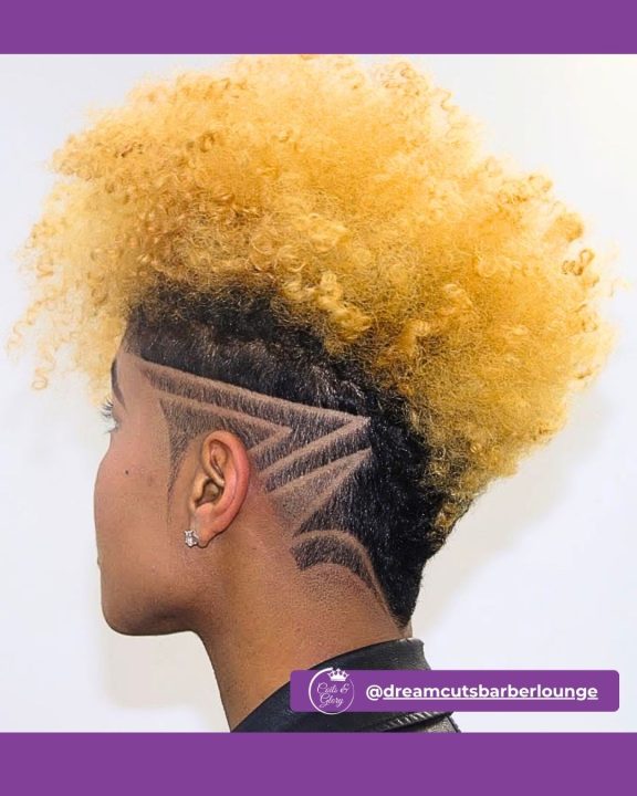 Vibrant bright blonde afro frohawk with dense texture on top, paired with low-faded sides etched with a sharp geometric razor design.