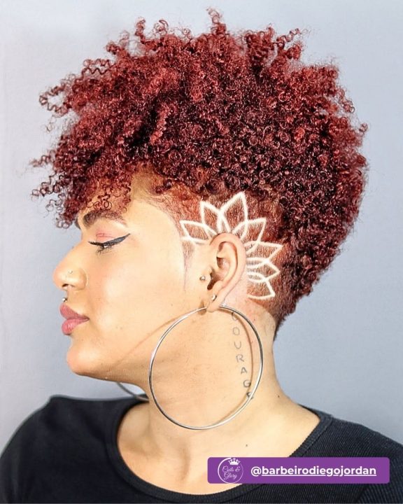 Burgundy coiled frohawk haircut featuring intricate lotus flower hair art on the faded side.