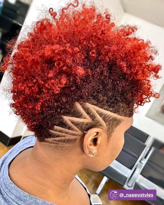 Defined copper-red ringlet curls styled in a tapered afro, contrasted with neatly faded sides carved with a sharp geometric razor design.
