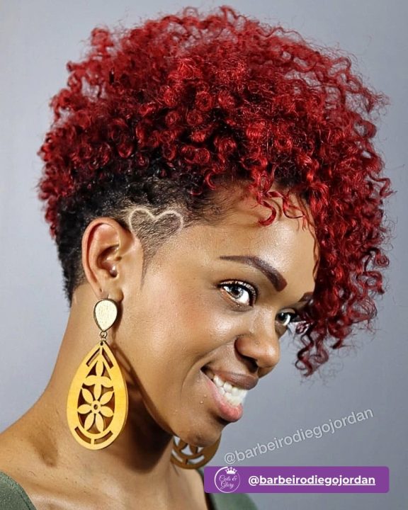 Vibrant crimson red coiled frohawk with defined natural texture on top, paired with low-faded sides etched with a sharp heart shaved pattern.