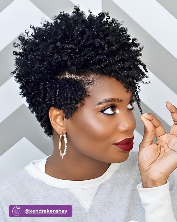 Deep jet black short afro pixie crop with defined natural texture on top, paired with neatly tapered sides and soft ringlet curls swept elegantly to the side.