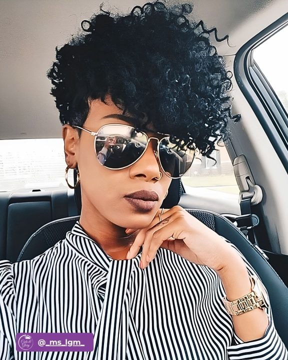 Deep jet black frohawk with defined ringlet curls swept gracefully to one side, contrasted with neatly tapered sides and a clean-cut nape.