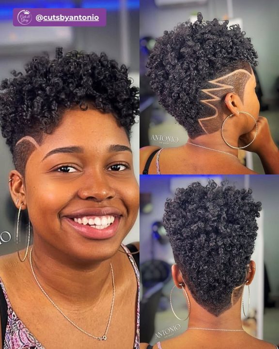 Deep jet black curly afro tapered closely along the sides and back, accented with a precise geometric razor pattern carved into the clean side fade.