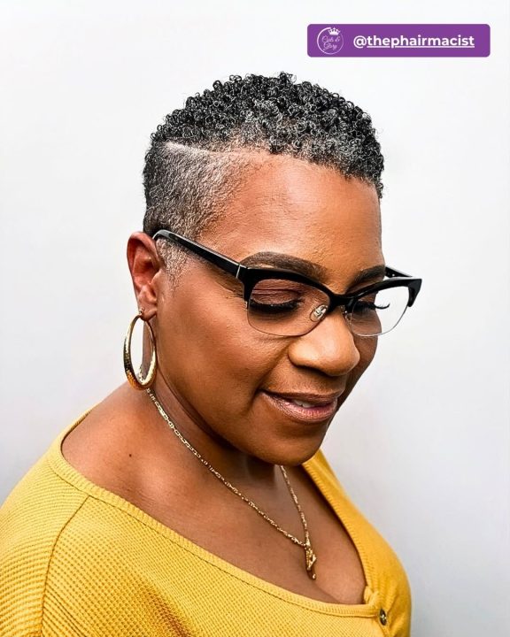 Natural grey-flecked short curly taper cut women's haircut with a razor parting line for short natural hair.